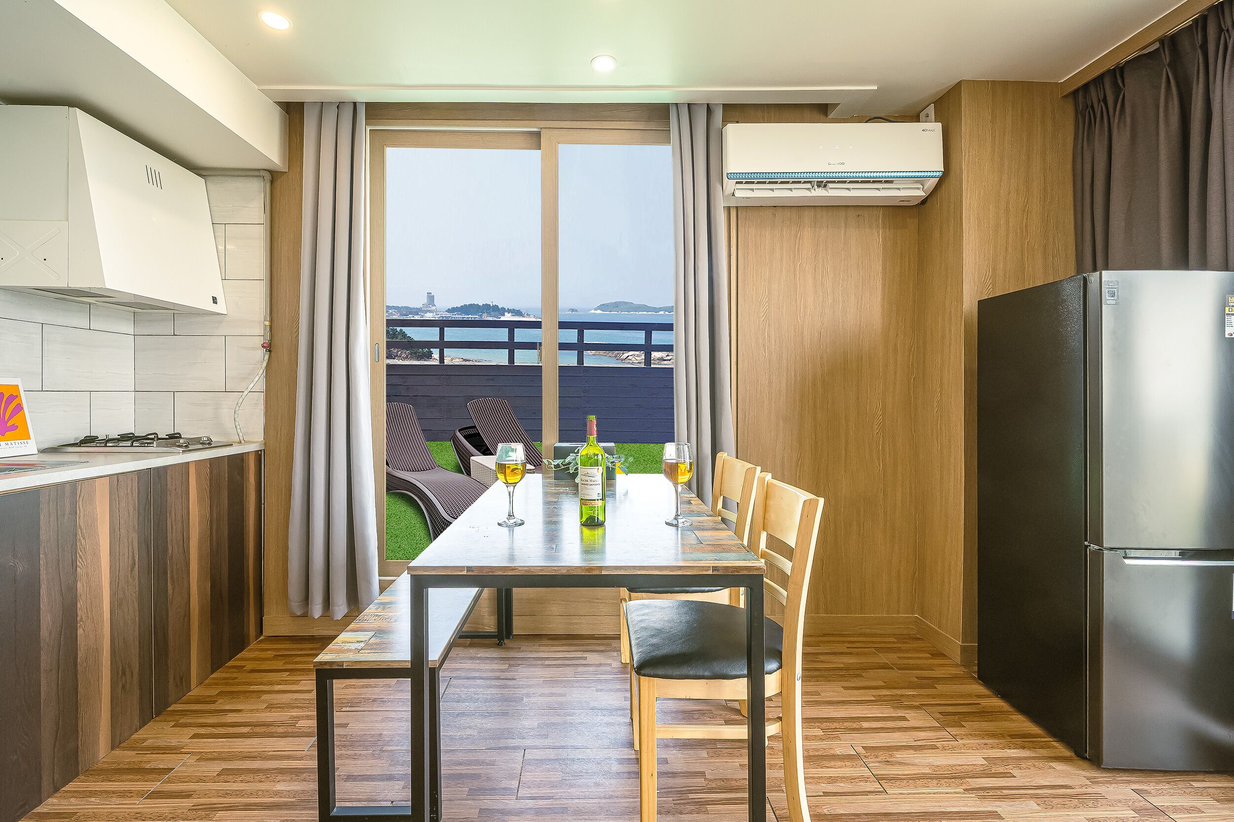 A modern kitchen with a dining area, a refrigerator, and a view of the sea.