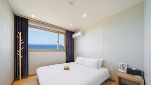 Habitación de hotel con una cama grande, vista al mar, una mesita de noche de madera y un equipo de aire acondicionado.