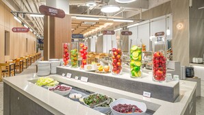 Zona de bufé con diversas opciones de comida, incluyendo ensaladas, frutas y platos calientes.