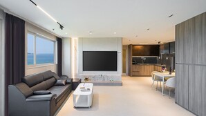 Una sala de estar moderna con un sofá, una mesa de centro y un televisor. Hay una cocina con una mesa de comedor y sillas.