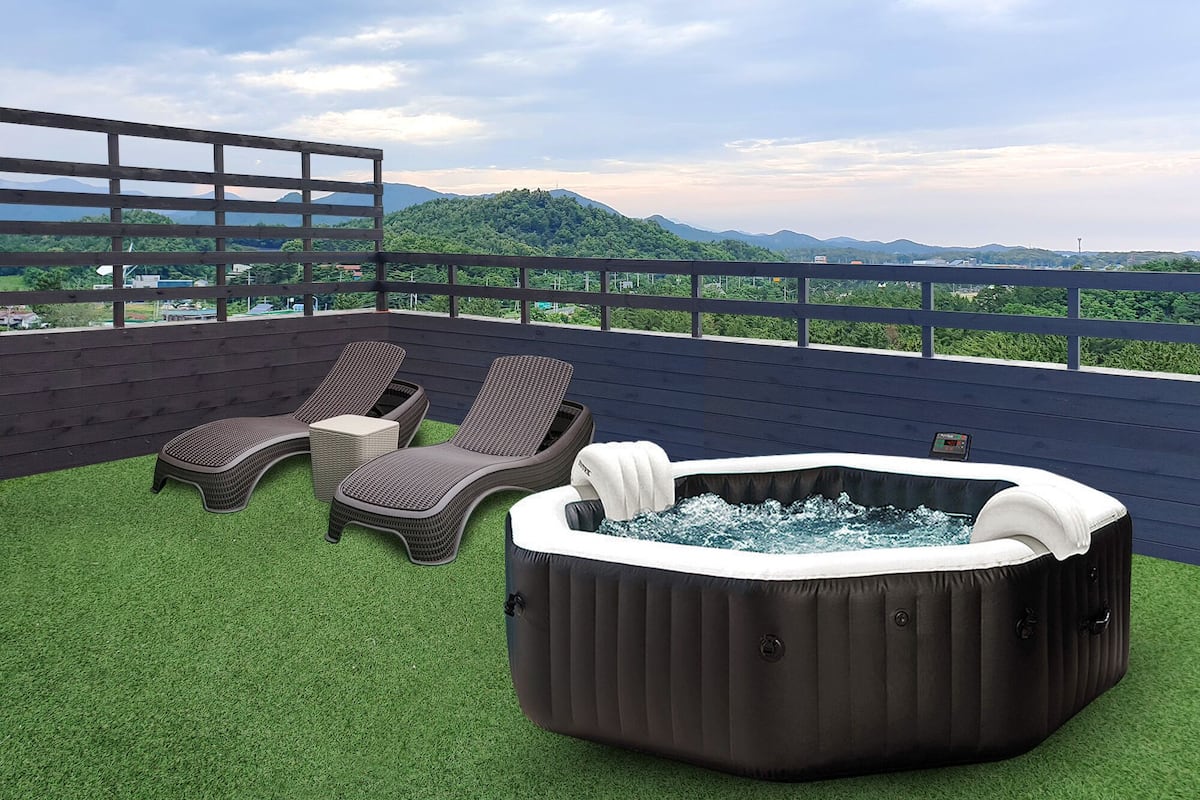 A rooftop terrace with two lounge chairs, a small table, and a hot tub.