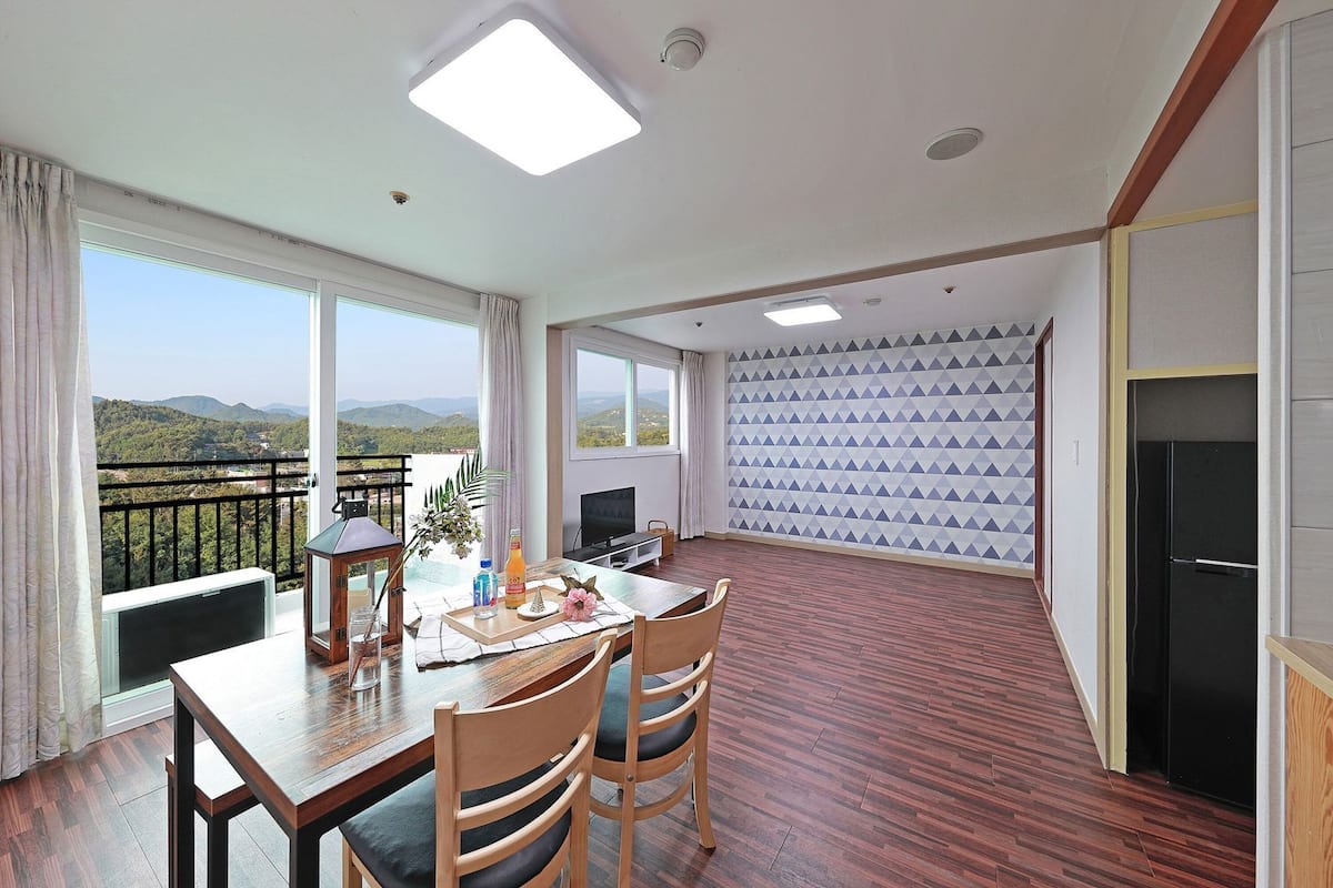 A spacious room with a balcony, a dining area with a table and chairs, a television, and a patterned wall.