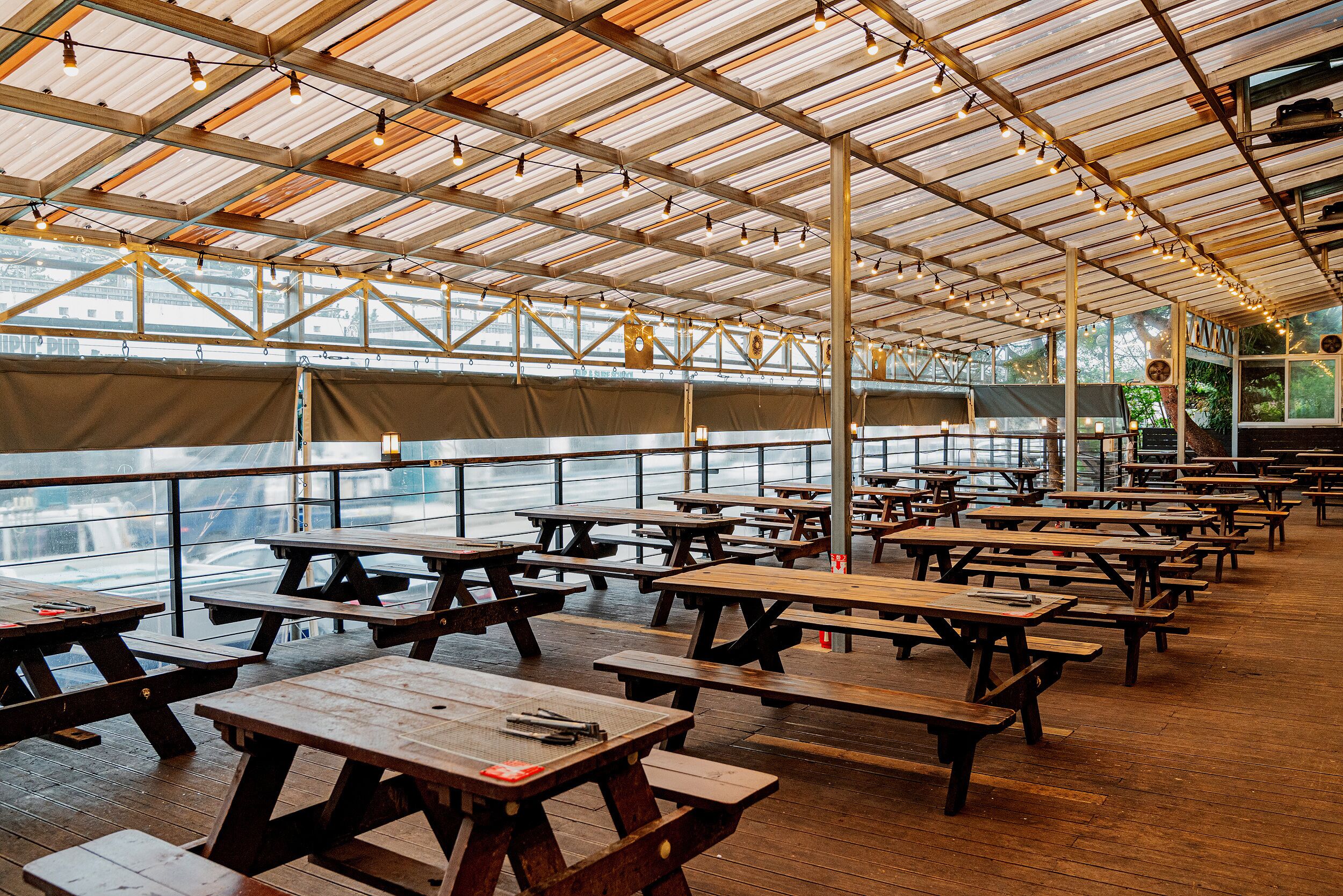 An indoor picnic area with wooden tables and benches, large windows, and a high ceiling with exposed beams.
