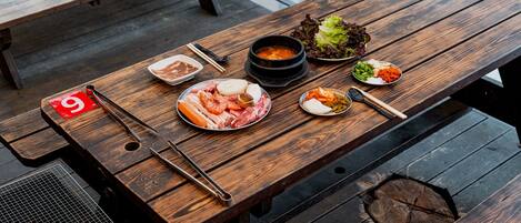 A wooden table with various dishes, chopsticks, and a grill.