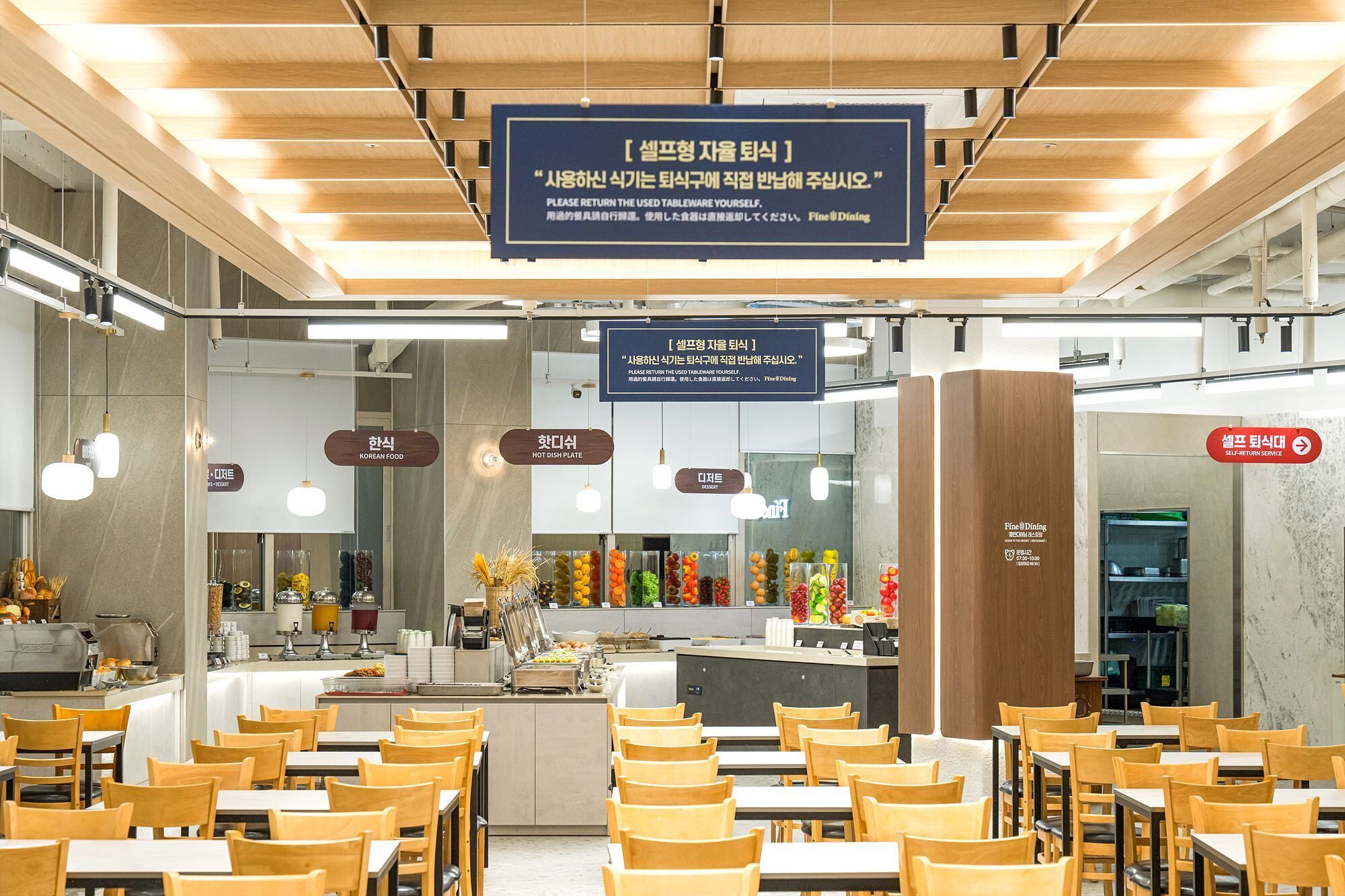Ein Restaurantinneres mit Tischen und Stühlen, einem Schild für die Selbstbedienung und Hinweisen auf koreanische Küche und heiße Speisen.