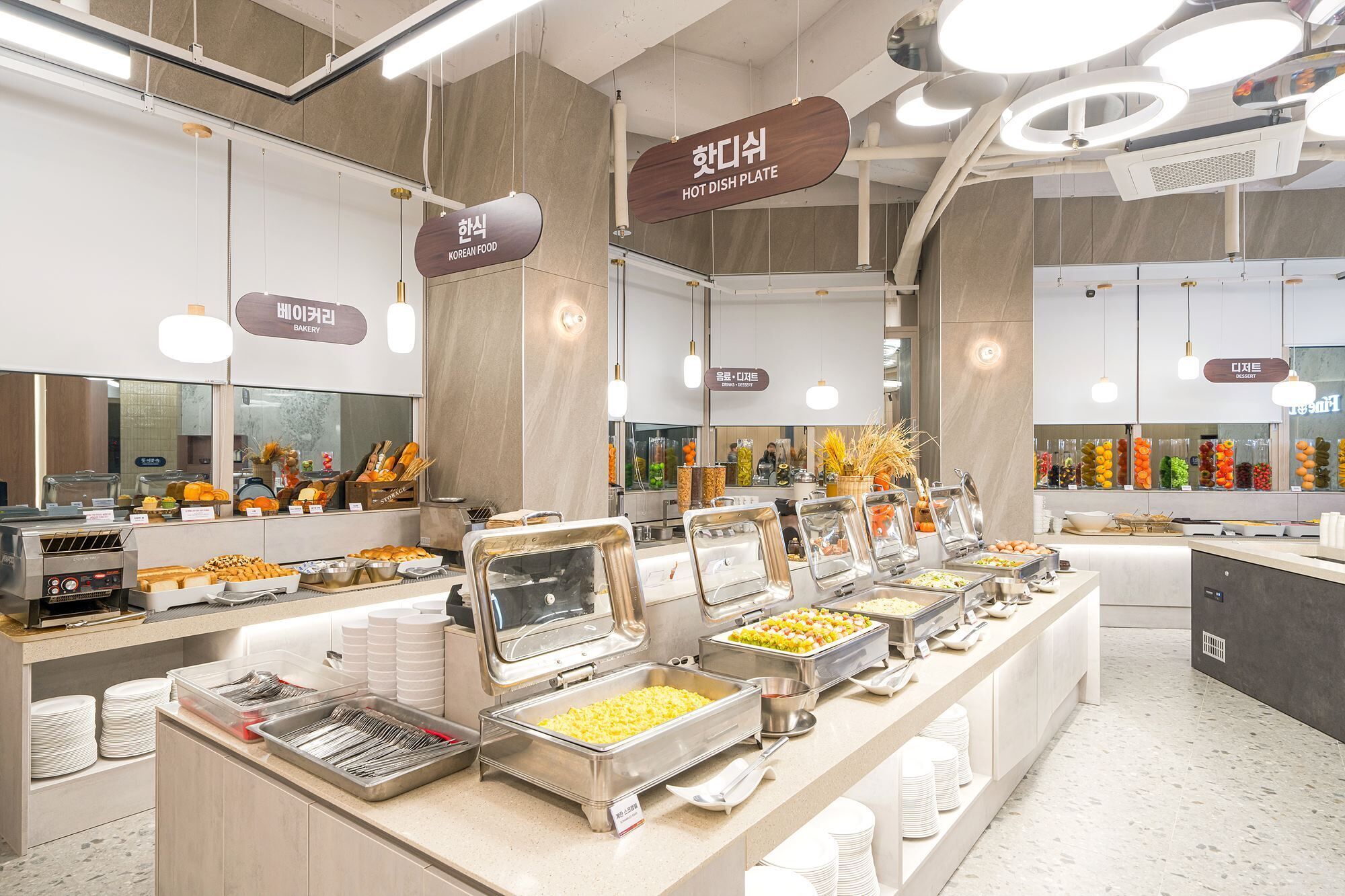 Un espace buffet proposant différents stands de restauration, notamment un coin dédié à la cuisine coréenne, une boulangerie et un espace réservé aux desserts.