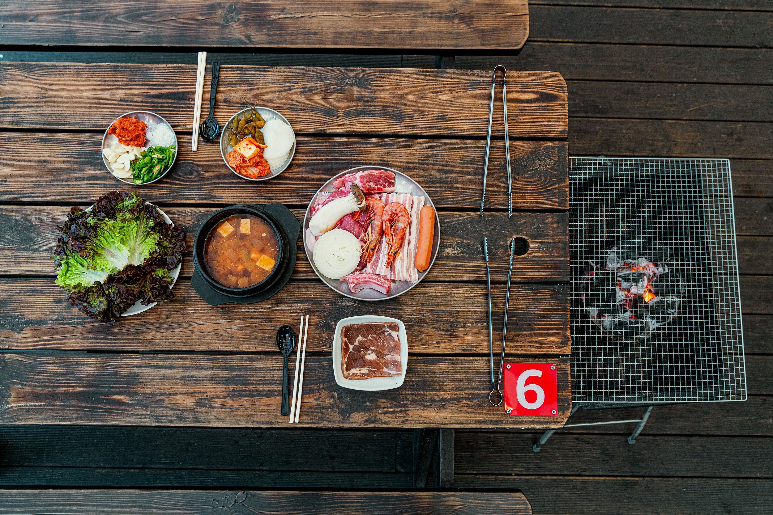A wooden table with various food items, chopsticks, and a grill.