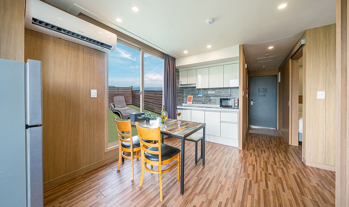 A modern kitchen with a dining area, wooden flooring, and a view of the outdoors.