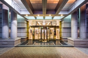 Entrada de hotel con puerta giratoria, amplias columnas y fachada de vidrio.