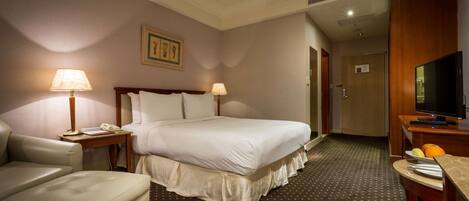 Una habitación de hotel con una cama, un escritorio con lámpara, una silla y un televisor.