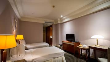 A hotel room with two beds, a desk with a TV, a desk lamp, a telephone, and a small table with a lamp.