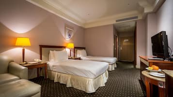 A hotel room with two beds, a desk with a lamp, a TV, and a chair.