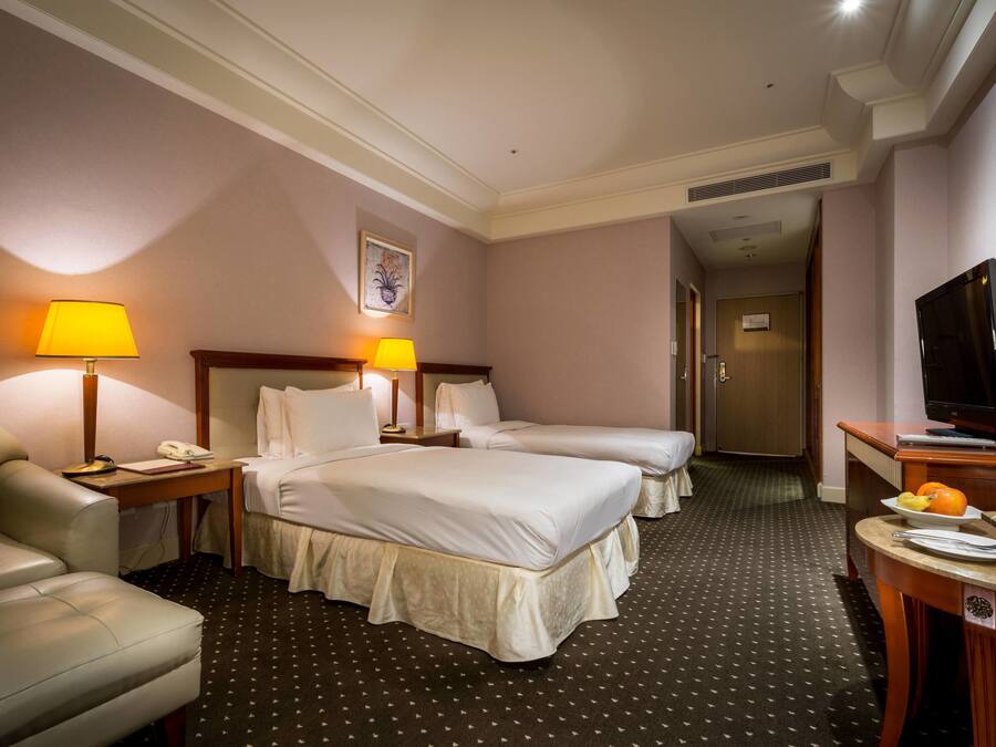 A hotel room with two beds, a desk with a lamp, a TV, and a chair.
