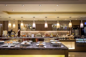 Un restaurante de hotel bien iluminado con mostrador de mármol, varias lámparas colgantes y una variedad de platos expuestos.
