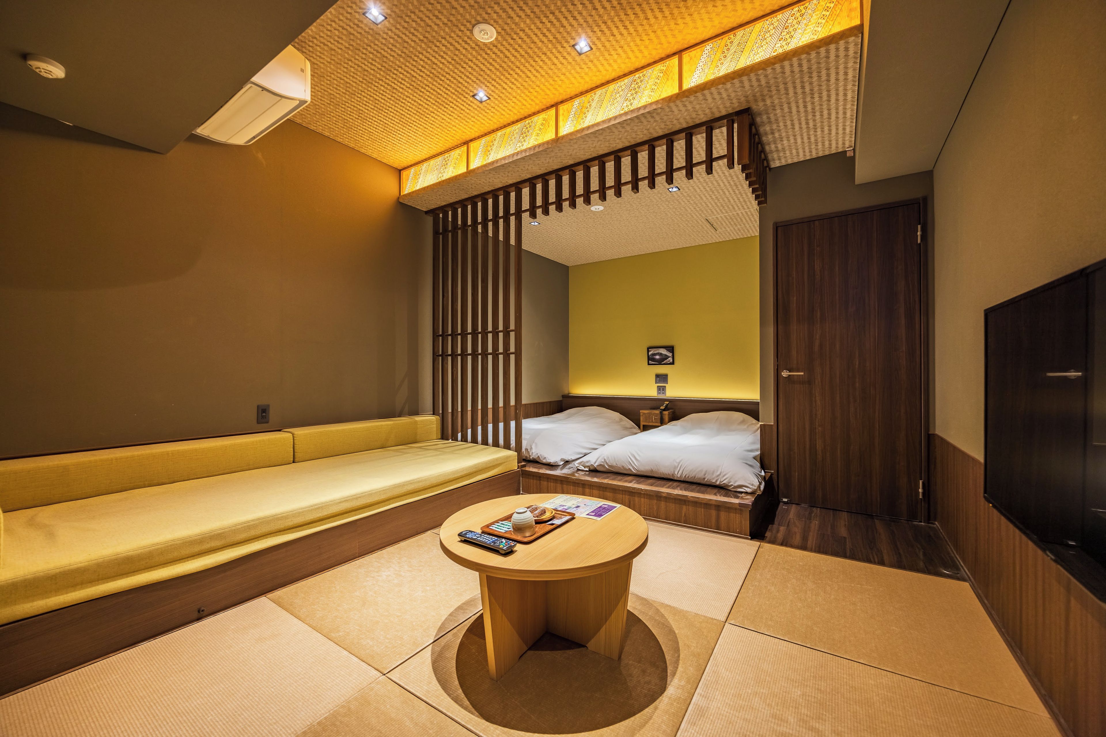 A hotel room with a sofa, a bed, a small table with a remote control, and a TV.