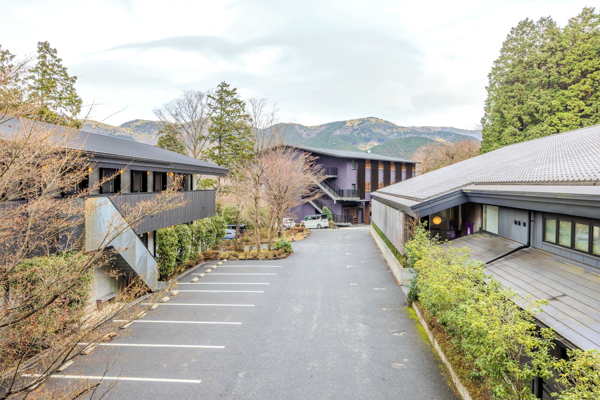 A modern building with a covered walkway, surrounded by trees and a mountainous backdrop.