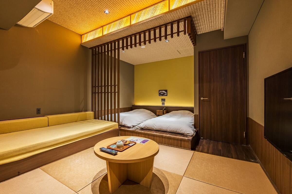 Ein Hotelzimmer mit einer Couch, zwei Betten, einem kleinen Tisch und einem Fernseher.