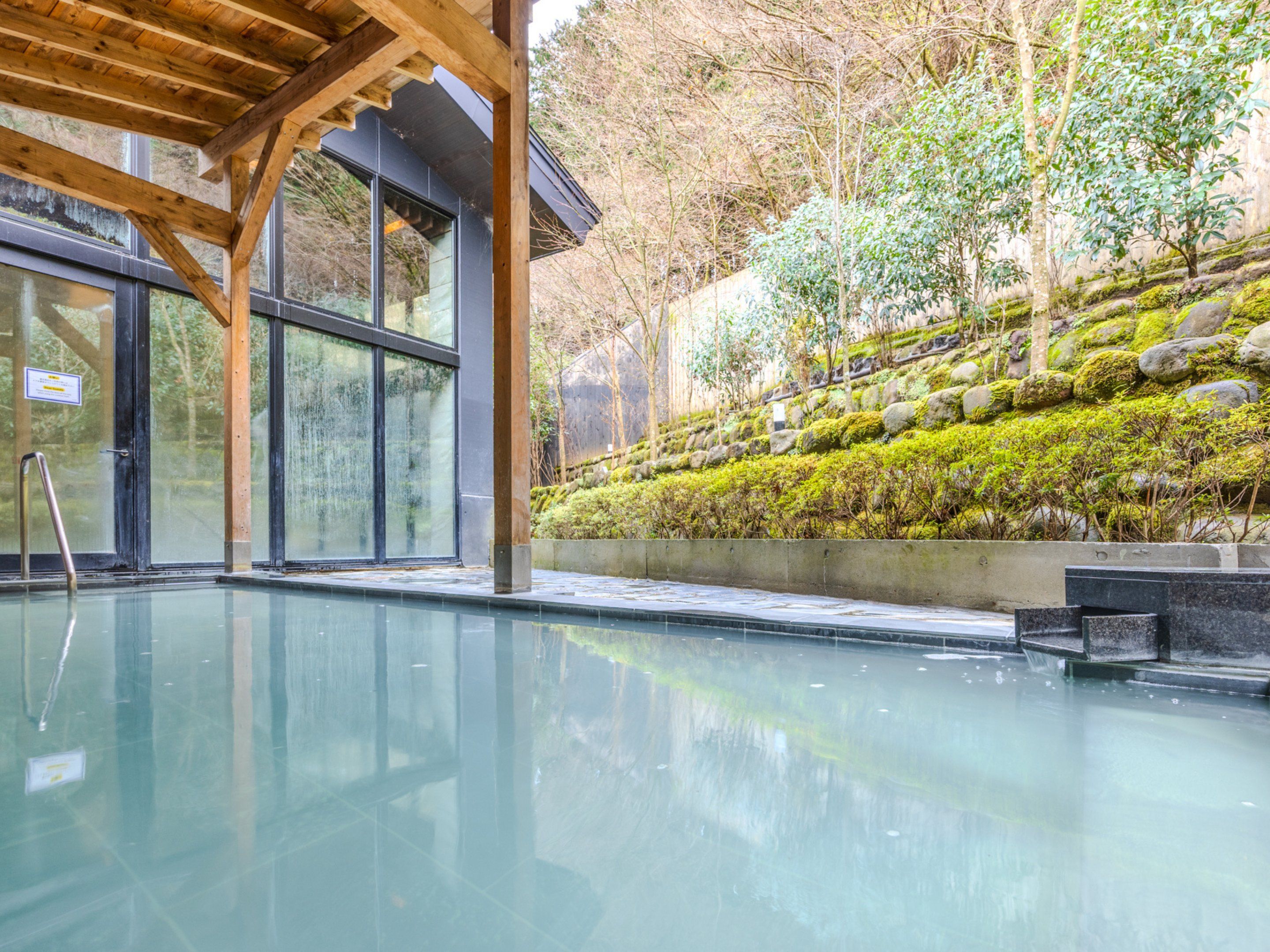 An indoor swimming pool with a wooden ceiling and glass doors, surrounded by a landscaped garden with rocks and greenery.