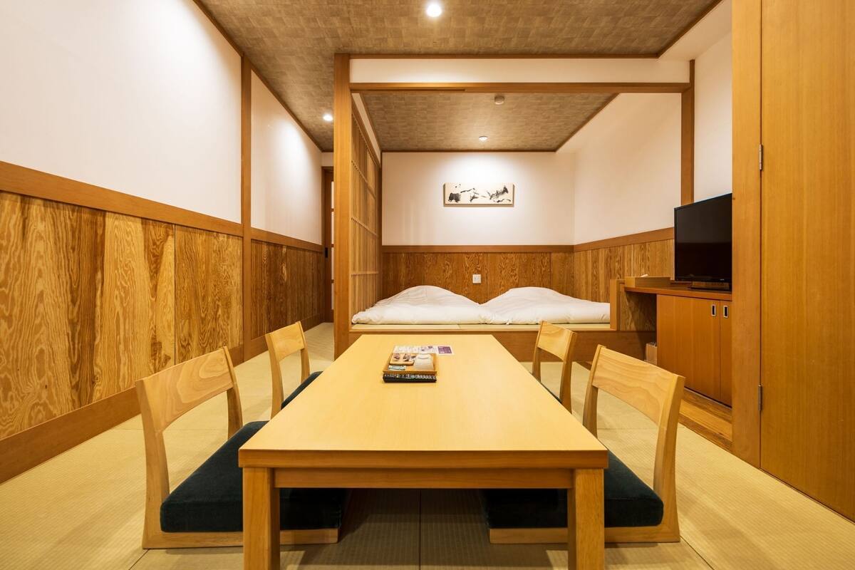Ein traditioneller japanischer Raum mit Holztisch, Stühlen, einem Bett und einem Fernseher.