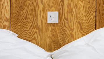 A wooden wall with a white electrical outlet and a white bed with white bedding.