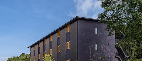 A modern building with a dark facade, vertical windows, and a staircase leading to an upper level.
