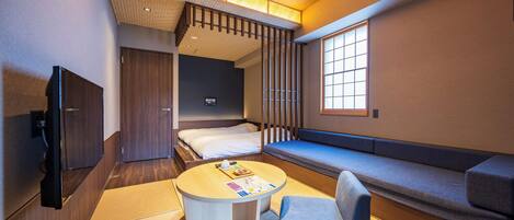 A compact hotel room with a bed, a seating area, a small table, and a TV.