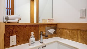 Un baño con un tocador de madera, un lavabo blanco, un espejo, un secador de pelo y una botella de jabón Lúcido.