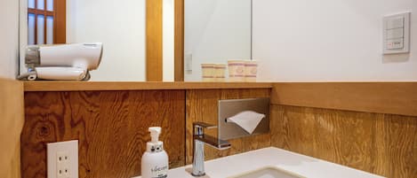 Casa de banho com toucador de madeira, lavatório branco, espelho, secador de cabelo e frasco de sabonete Lúcido.