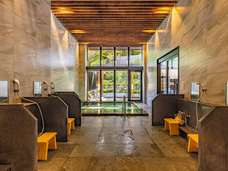 Un moderno espacio de spa con paredes de piedra, bancos de madera y una bañera de hidromasaje con cerramiento de vidrio.