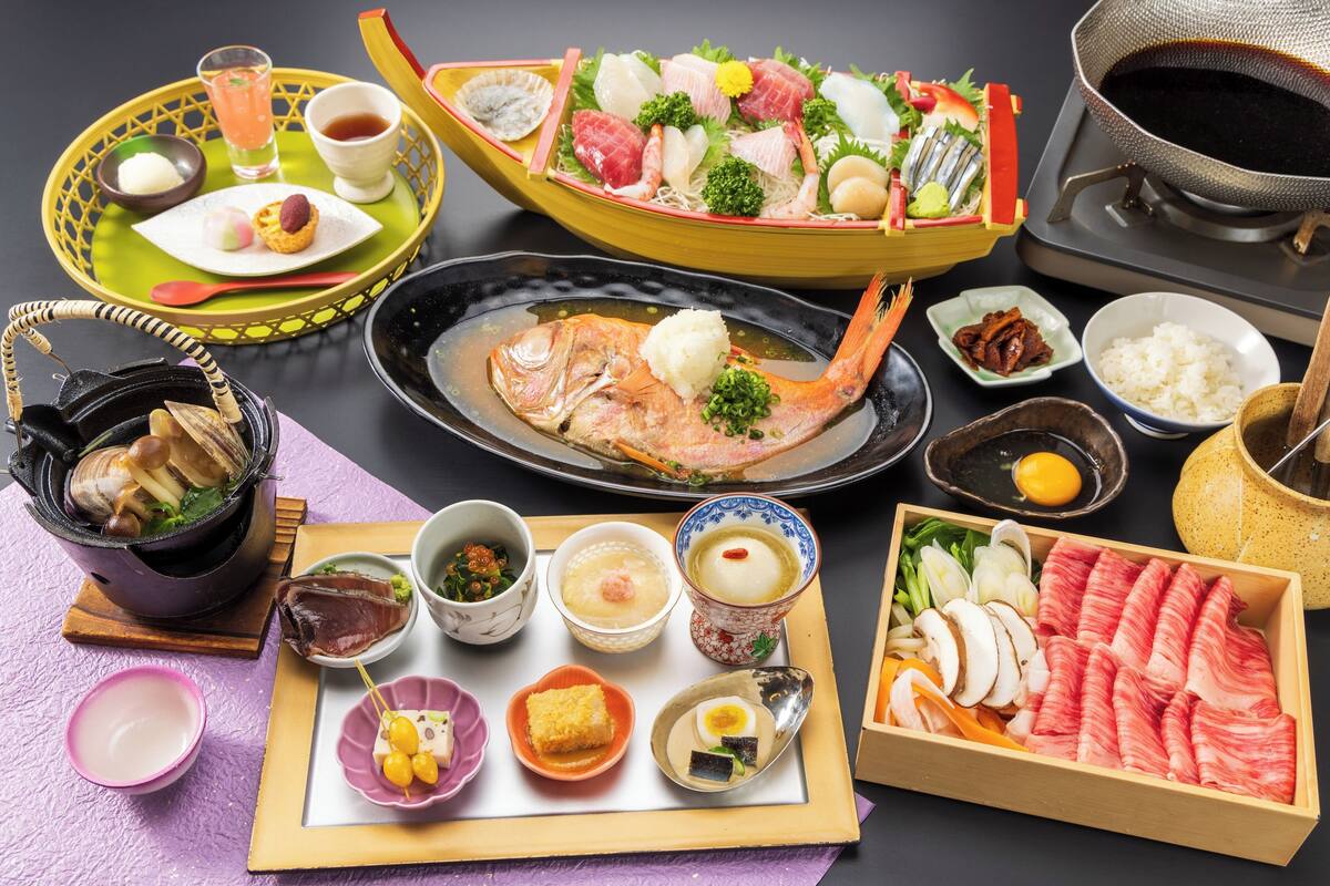 Verschiedene japanische Gerichte, darunter Sushi, Sashimi und gegrillter Fisch, serviert auf einer Holzschale.