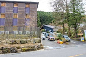 Un estacionamiento con varios autos, un edificio con listones de madera verticales y un muro de piedra con rocas.