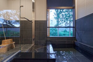 A modern bathroom with a glass shower enclosure, a bathtub, and a window with a view of trees.