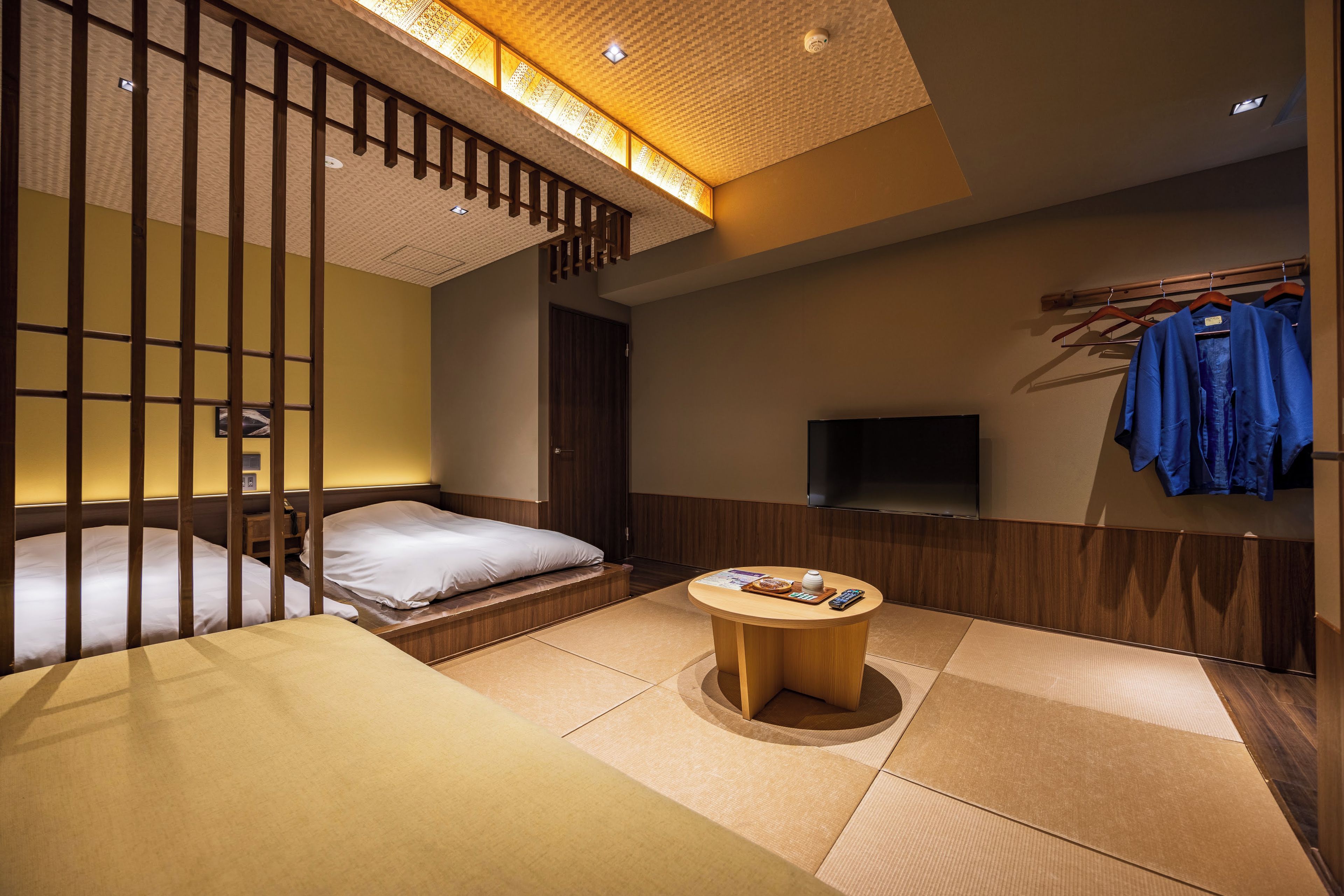 A hotel room with a bed, a small table with a remote control, a TV, and a clothing rack with hangers.