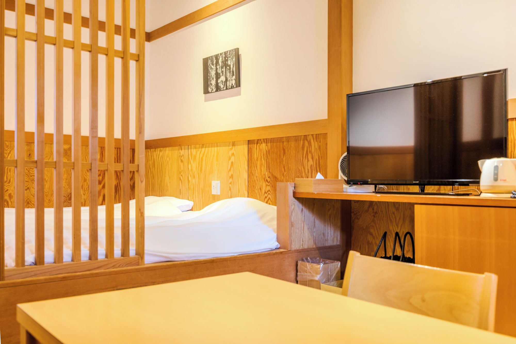 Una habitación de hotel con cama, televisor, escritorio de madera y un cuadro colgado en la pared.
