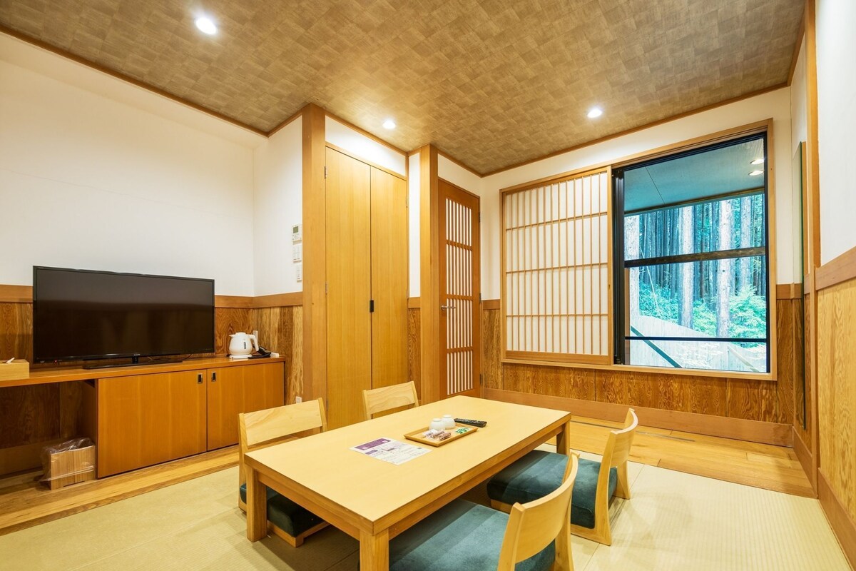 Una habitación tradicional japonesa con suelo de tatami, una mesa baja con cojines, un televisor y puertas correderas.