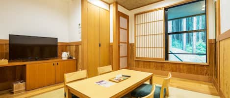 A traditional Japanese-style room with tatami flooring, a low table with cushions, a television, and sliding doors.