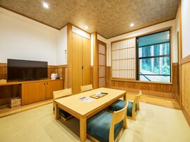 Una habitación tradicional japonesa con suelo de tatami, una mesa baja con cojines, un televisor y puertas correderas.
