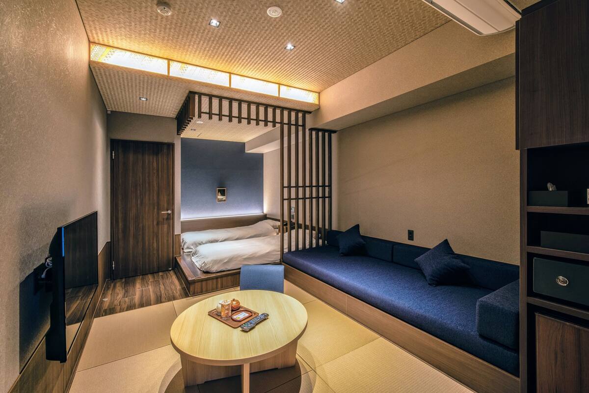 Ein modernes Hotelzimmer mit einer Couch, einem kleinen Tisch mit einer Auswahl an Snacks, einem Bett und einem Fernseher.