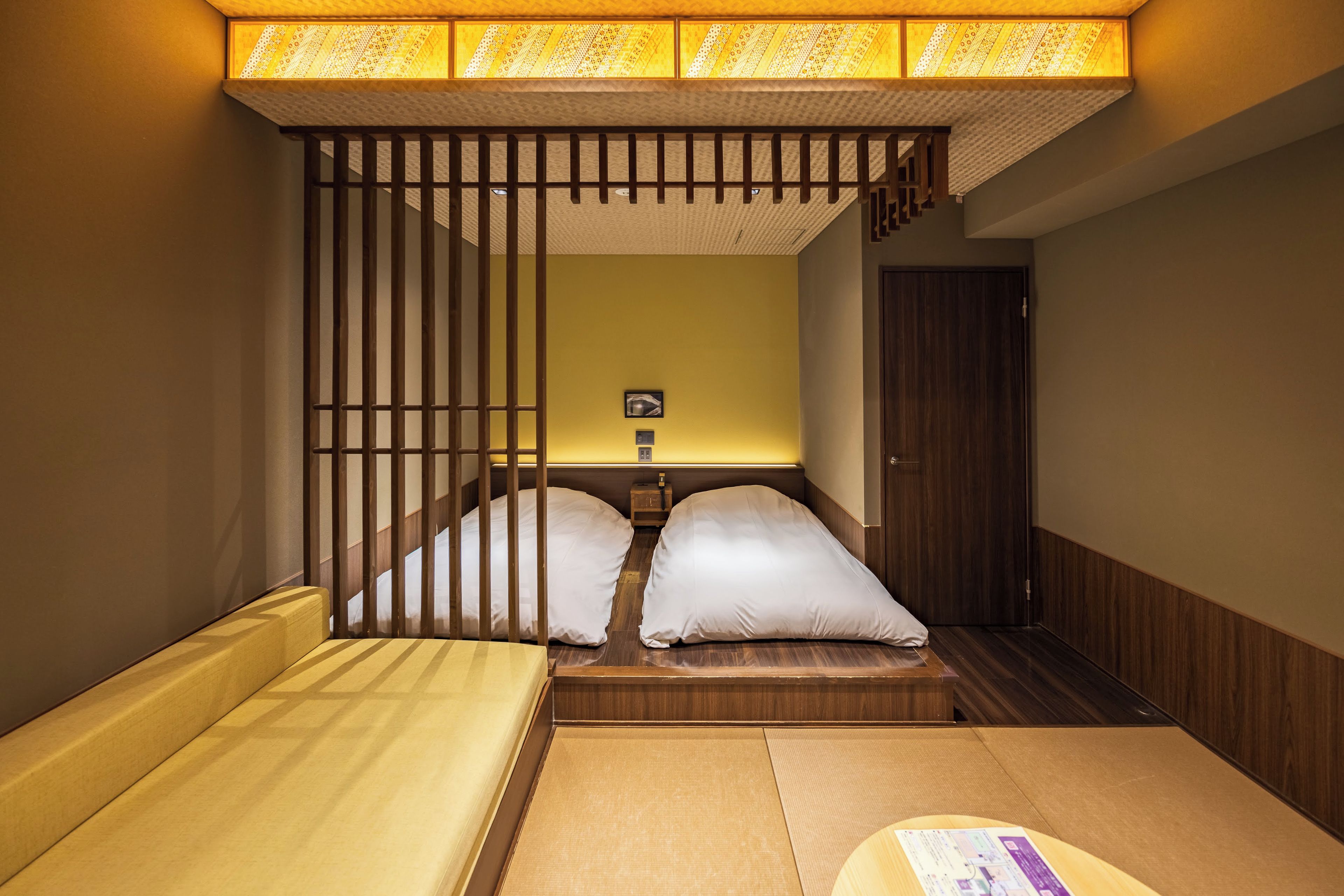 A traditional Japanese-style room with tatami flooring, a low wooden bed with white bedding, and a sliding shoji screen door.