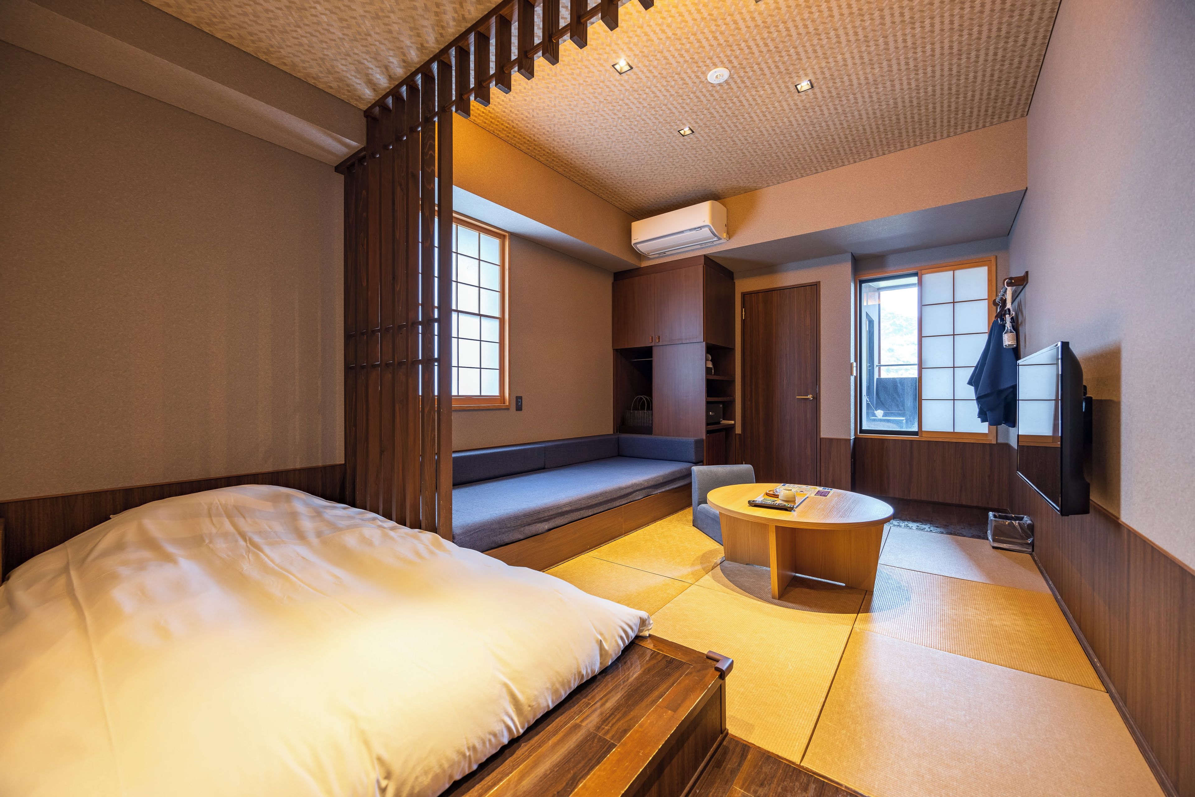 A traditional Japanese-style room with tatami flooring, a low wooden bed, a small round table, and a sliding door.