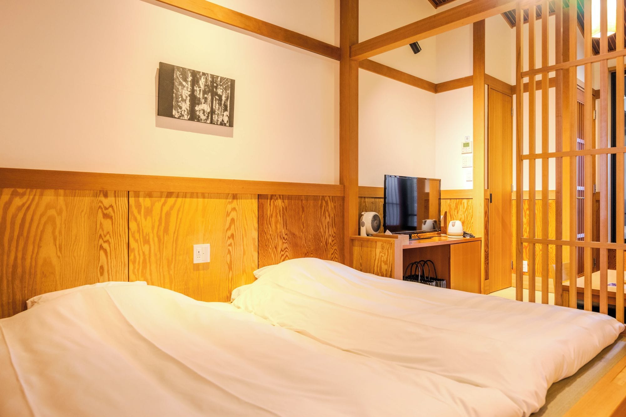 A hotel room with a bed, a desk with a computer, and a traditional Japanese sliding door.