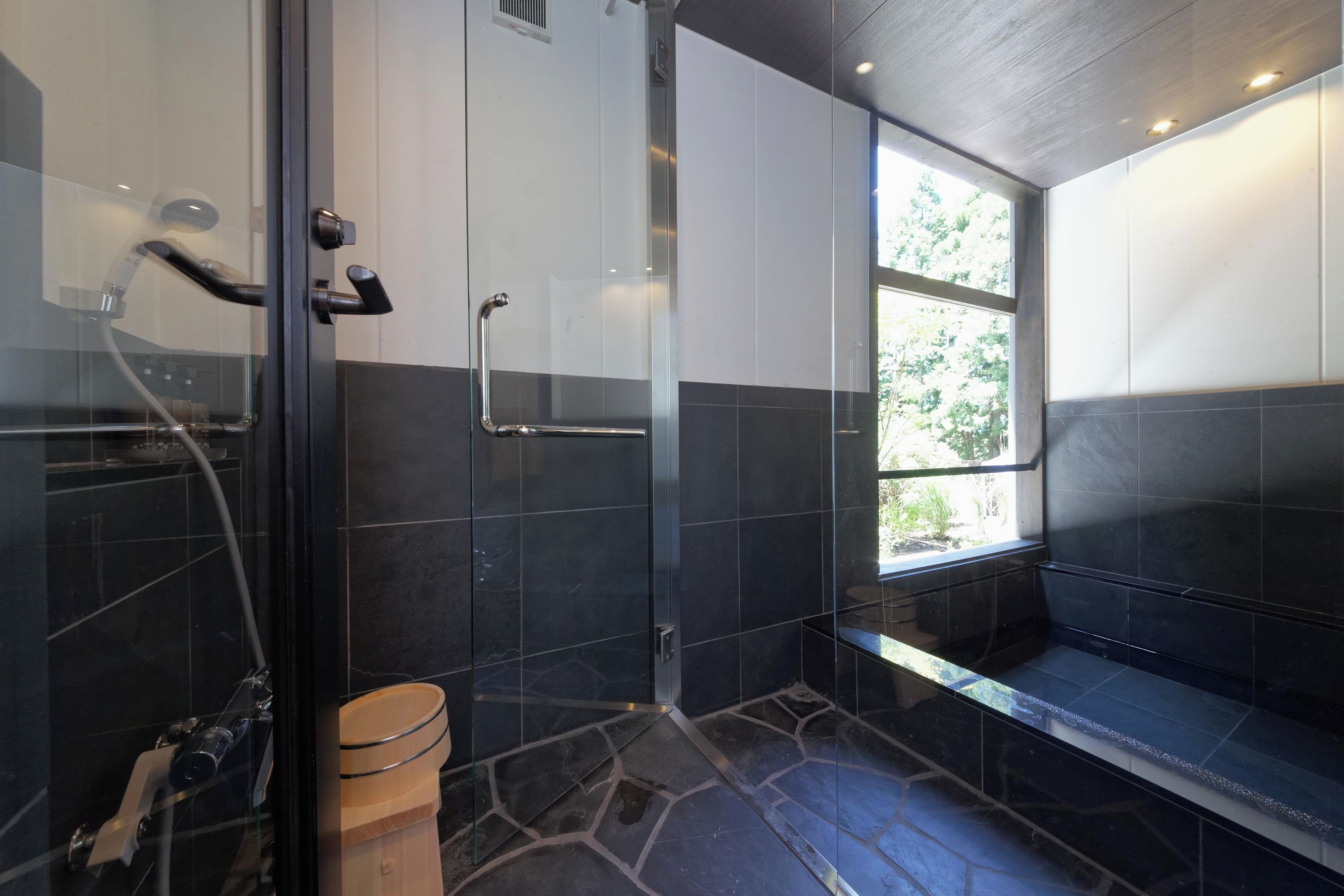 A modern bathroom with a glass shower enclosure, a wooden bench, and a window providing natural light.