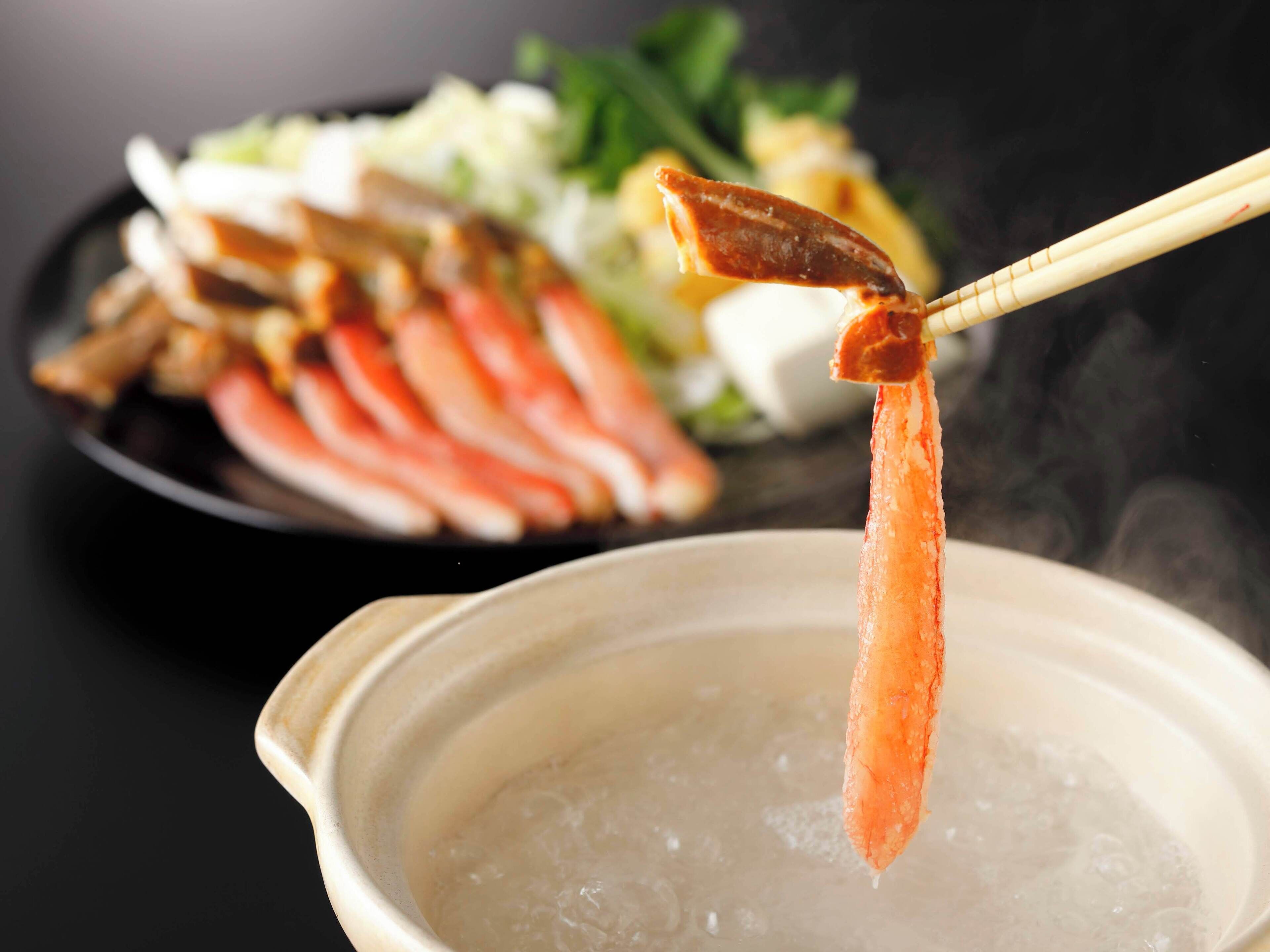 A bowl of soup with a piece of salmon on a chopstick.