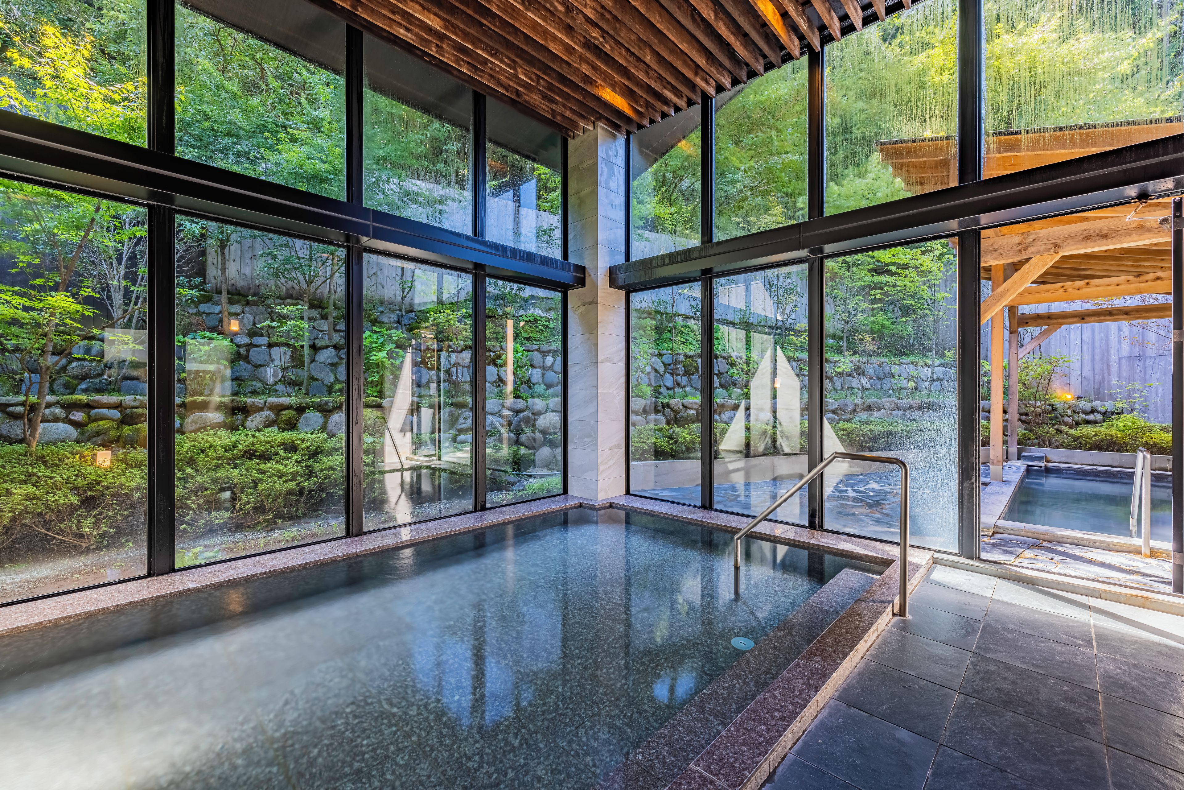 A modern indoor pool with large windows, stone walls, and a wooden ceiling.