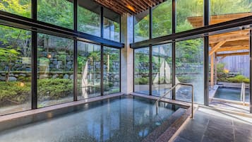 A modern indoor pool with large windows, stone walls, and a wooden ceiling.