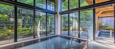 A modern indoor pool with large windows, stone walls, and a wooden ceiling.