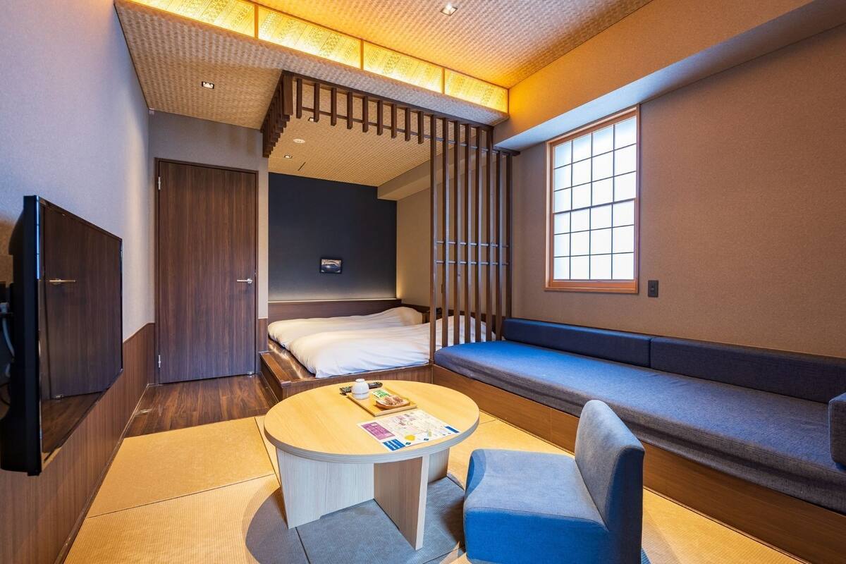 A compact hotel room with a bed, a seating area, a small table, and a TV.