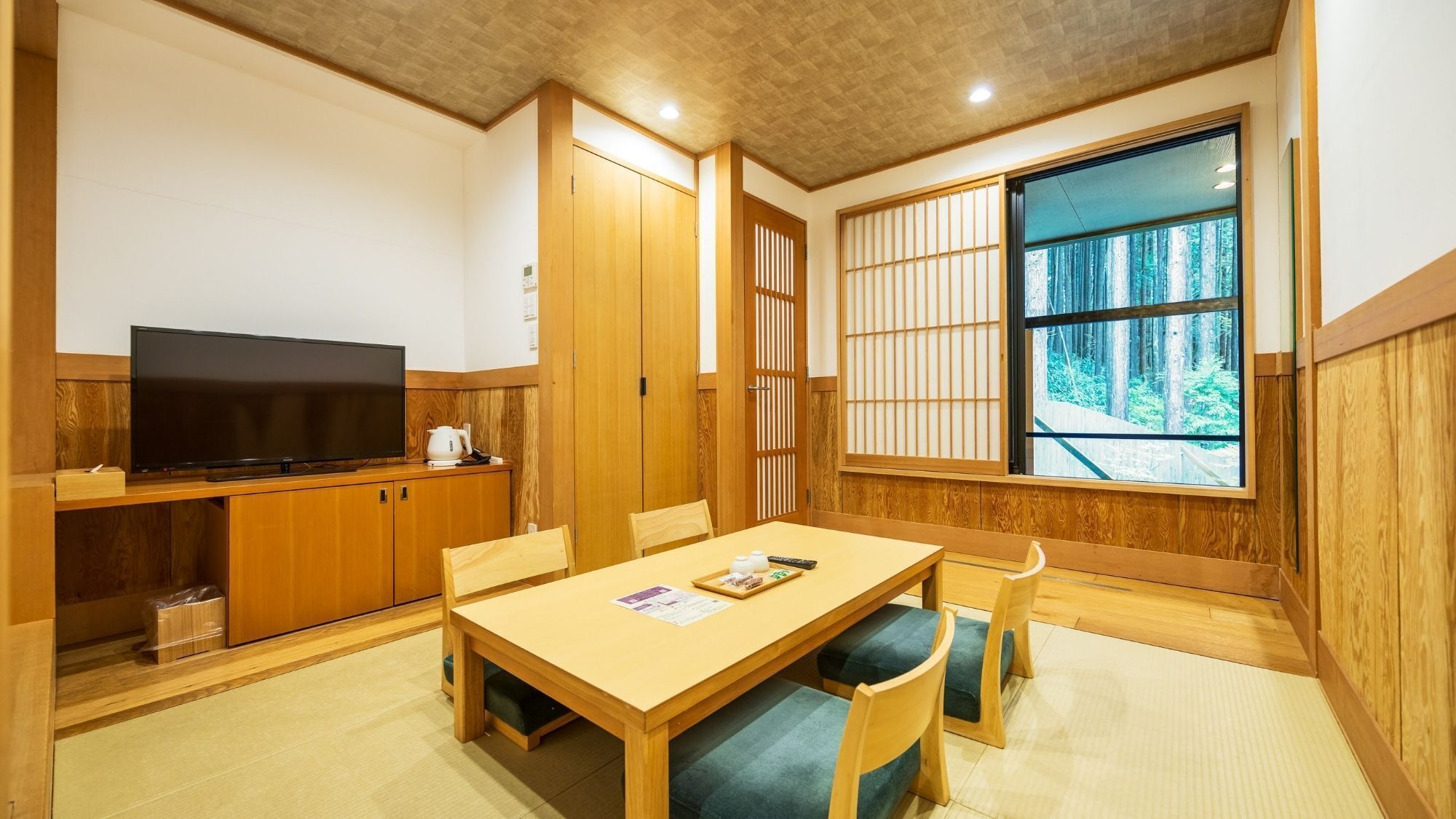 Une pièce de style japonais traditionnel, avec un sol recouvert de tatamis, un téléviseur, un meuble en bois et une porte coulissante.