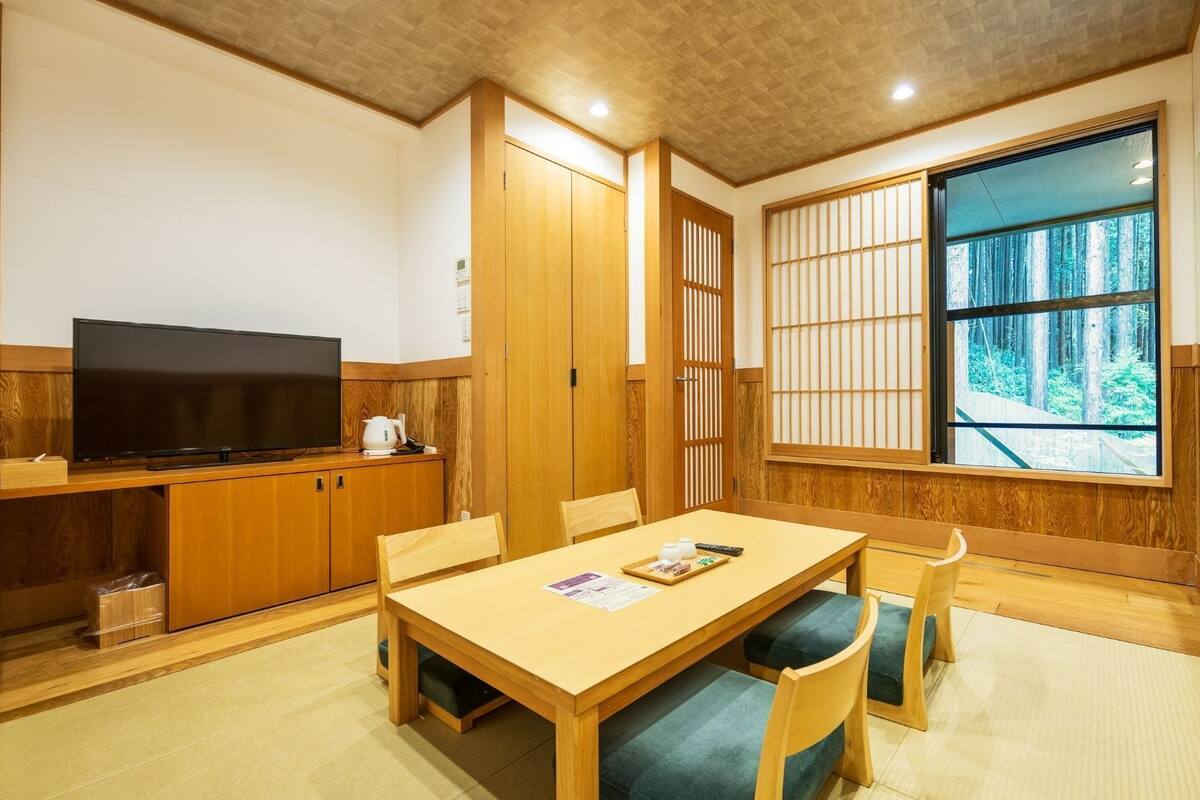 Ein traditioneller japanischer Raum mit Tatami-Boden, einem Fernseher, einem Holzschrank und einer Schiebetür.