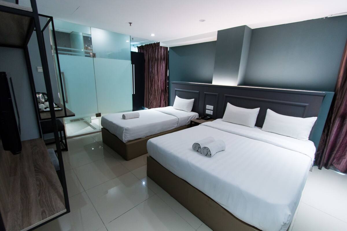 Habitación de hotel con dos camas individuales, un escritorio de madera, un separador de vidrio y un diseño moderno.